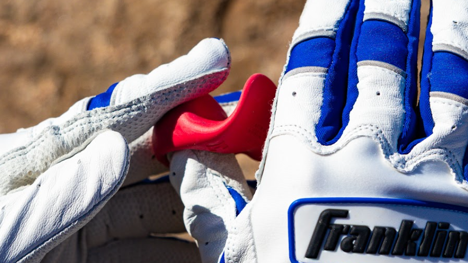 Putting a red launchpad thumb guard onto a hand with a white and blue batting glove