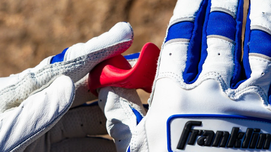Putting a red launchpad thumb guard onto a hand with a white and blue batting glove